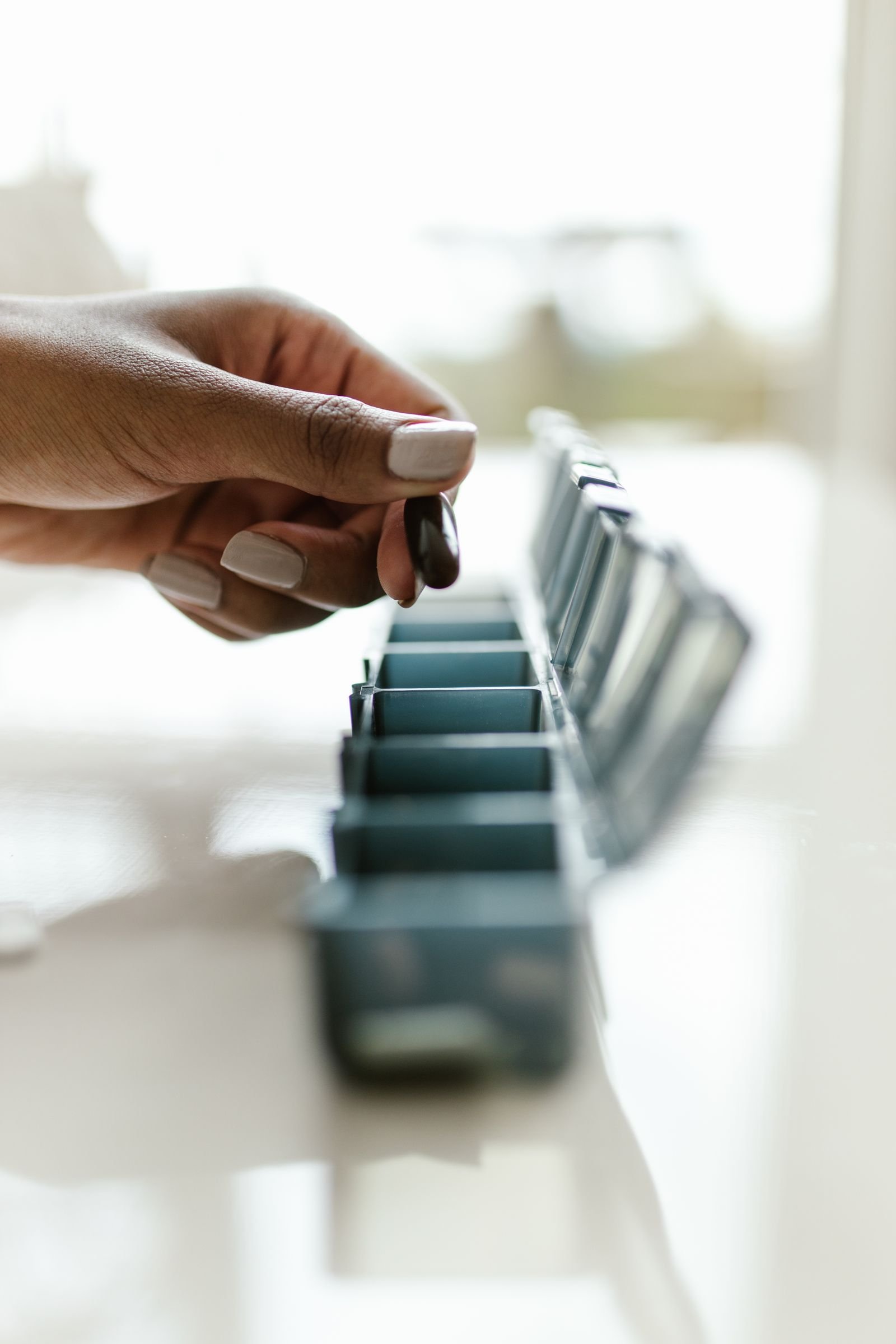 A hand placing medication into a weekly pill organizer