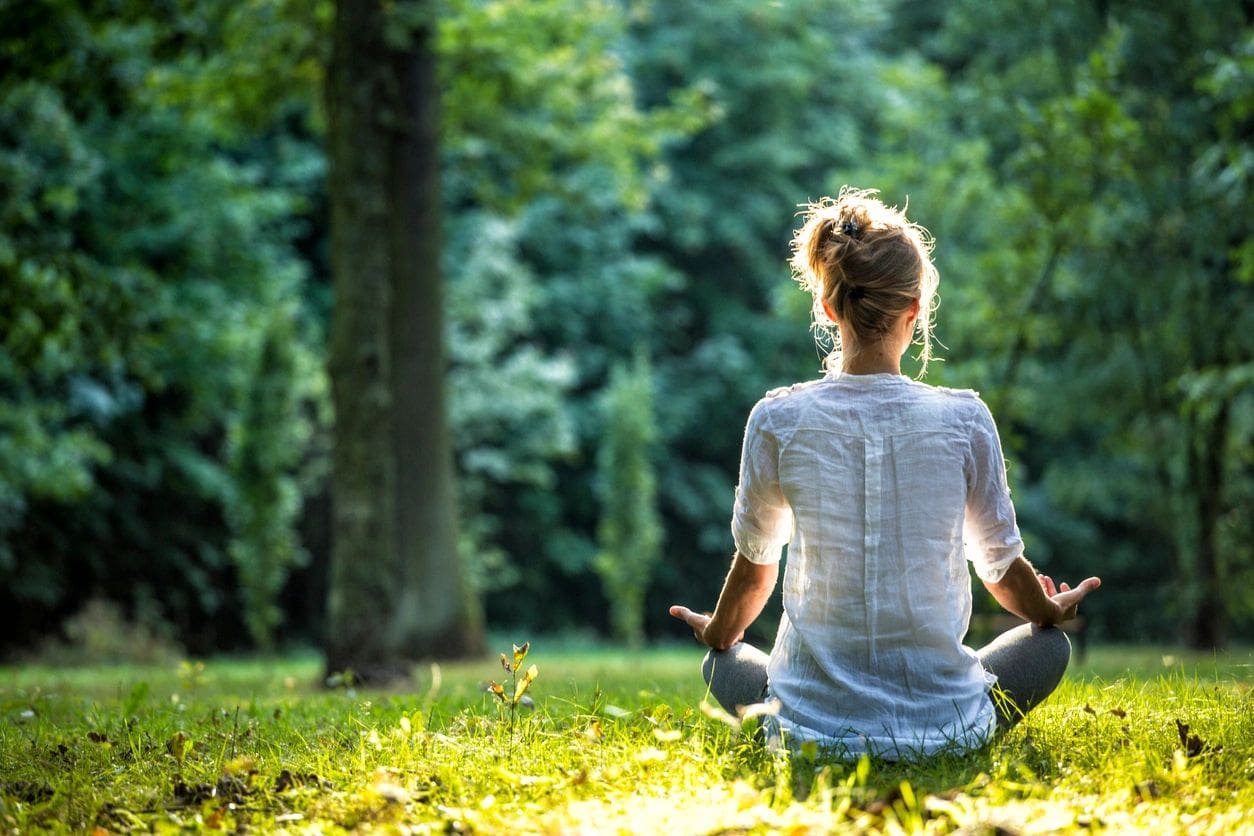 A woman sitting in the grass with her hands in yoga pose.