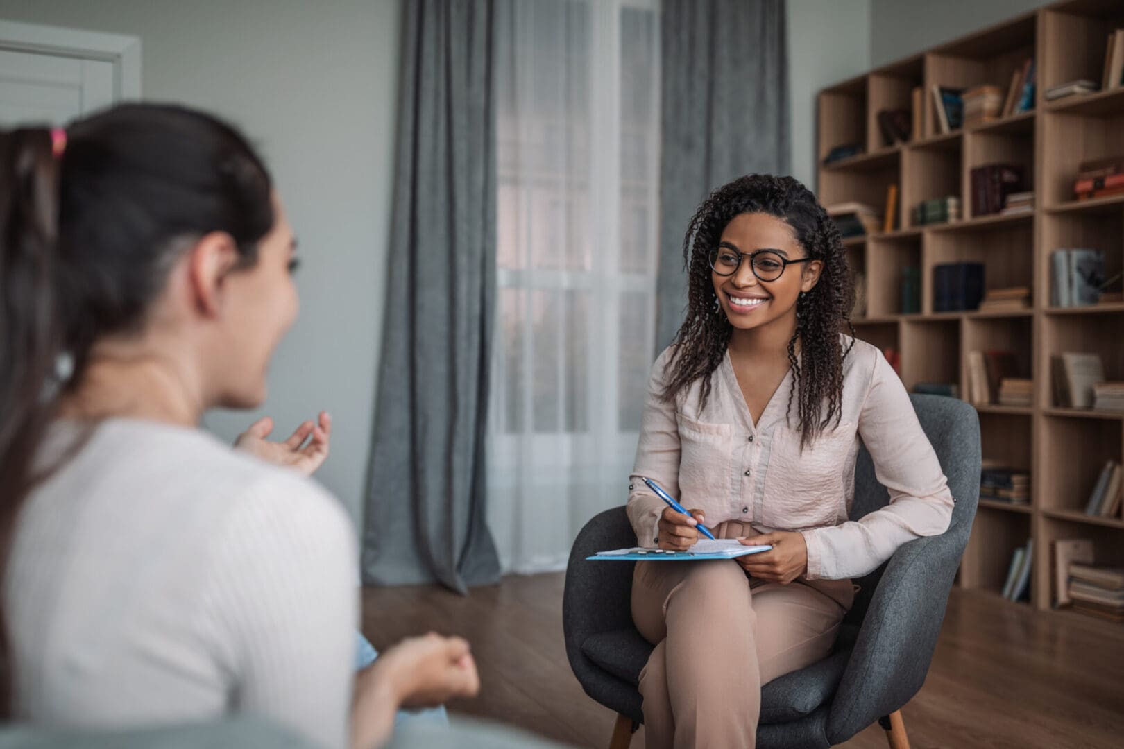 Smiling young black female doctor psychologist consulting european woman in modern clinic interior. Mental health care, medical support, psychological problems, therapy and professional treatment